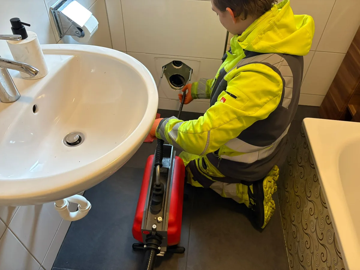 Techniker von HRR Rohrreinigung führt die Rohrreinigungsspirale in die Reinigungsöffnung neben dem Waschbecken ein